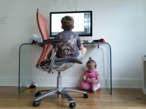 Foto: Ein Kind sitzt vorm PC am Schreibtisch, ein anderes sitzt unterm Schreibtisch