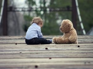 Foto: Kleinkind sitzt mit seinem Teddy auf einer Brücke