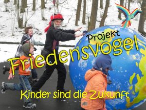 Foto: Micha rollt mit Kindern die Erdkugel durch die Schneelandschaft mit der Aufschrift: 'Projekt Friedensvogel - Kinder sind die Zukunft'